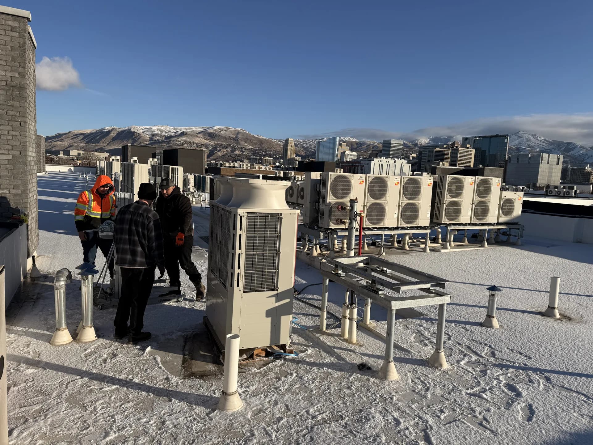 The All Around crew setting a rooftop heat pump above the Salt Lake City skyline